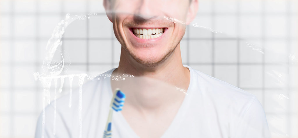 Young man stands in front of the mirror with freshly brushed teeth