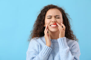 African-American woman with swollen gums around tooth on color background