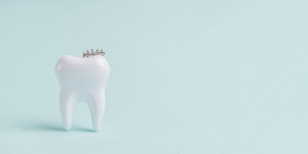 How long do crowns last - White tooth in crown on blue background with copy space