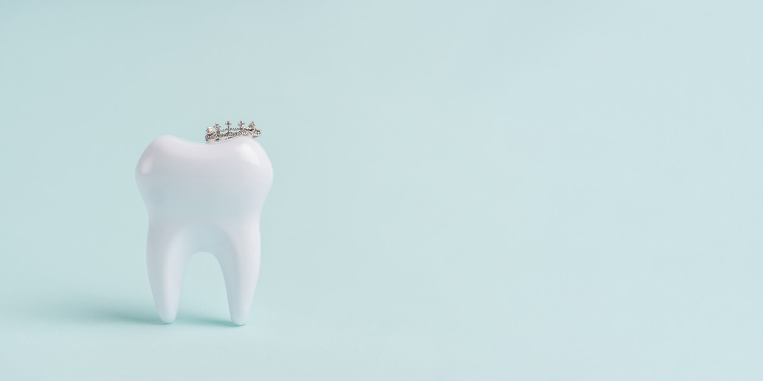 Weißer Zahn mit einer kleinen Krone auf einem hell blauen Hintergrund