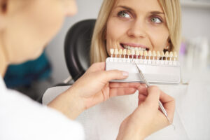 Zahnarzt bestimmt die Zahnfarbe einer Patientin mit einer Zahnfarbskala
