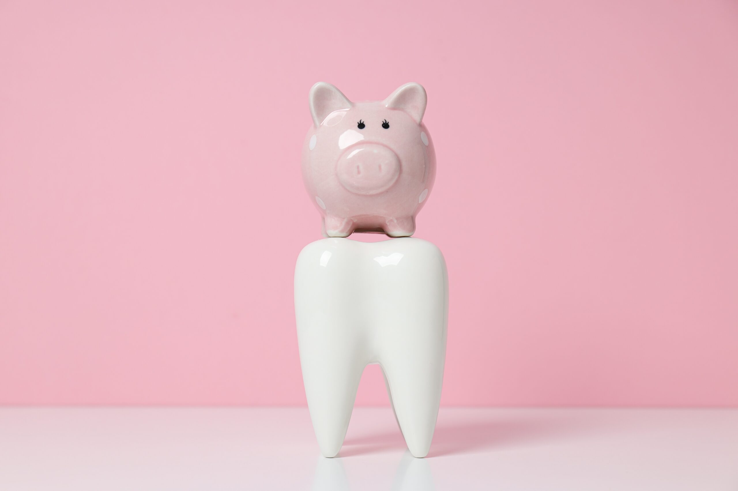 Preise für Zahnbehandlungen in der Türkei; künstlicher Zahn mit Sparschwein auf einem pinken Hintergrund