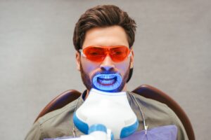 Junger Mann mit Bart sitzt beim Zahnarzt bei einem Laser Bleaching